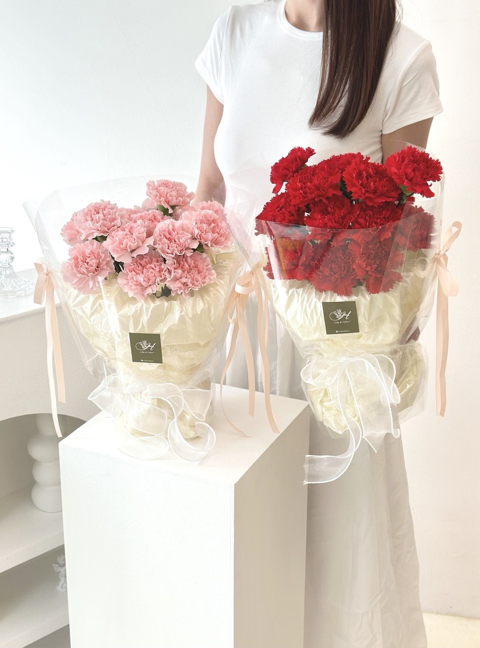 A girl in a white top holds pink and red carnation bouquets, celebrating Mother's Day 2026.