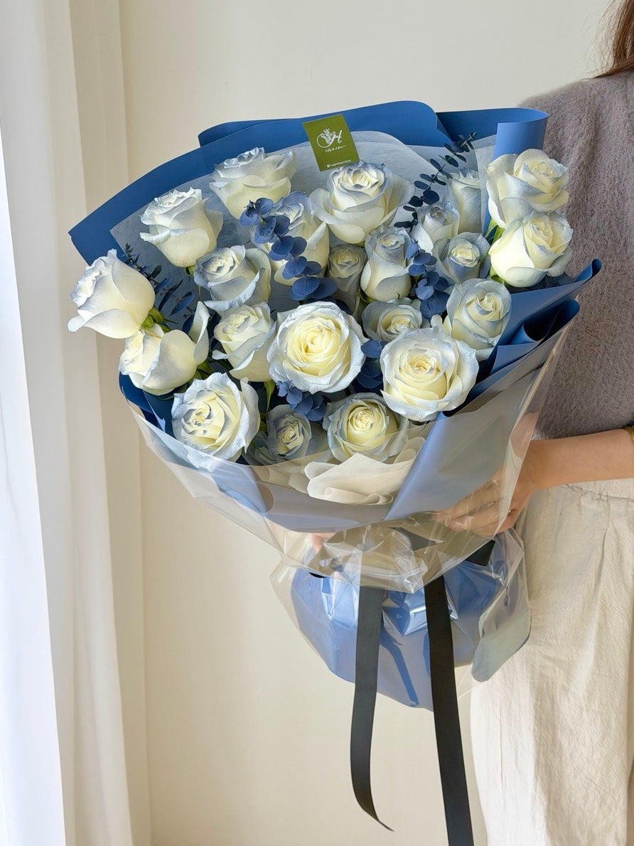 Bouquet of white roses with blue accents held by a person against a neutral background - same day delivery at Kuala Lumpur and Selangor.