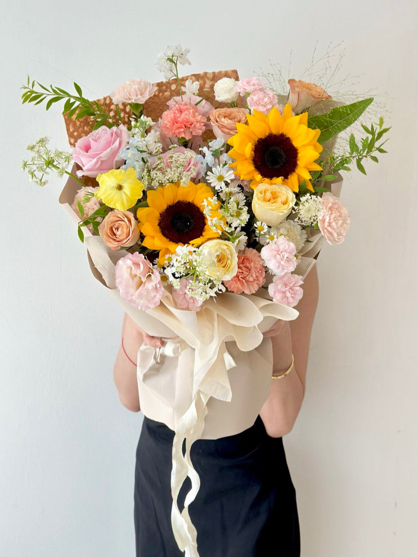 Vibrant sunflower bouquet mixed with pastel roses and carnations, ideal gift for a proud university graduate."