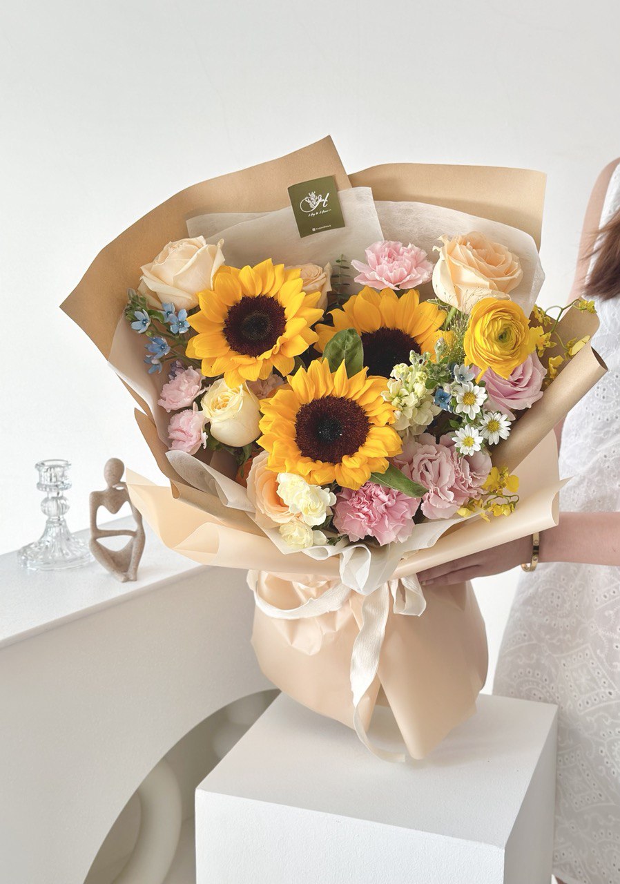 A graduate in a white dress proudly holds a bouquet of sunflowers, symbolizing her achievement.