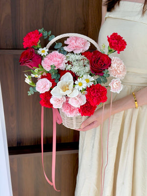 Bouquet of red, pink, and white flowers in a basket held by a person wearing a beige dress.