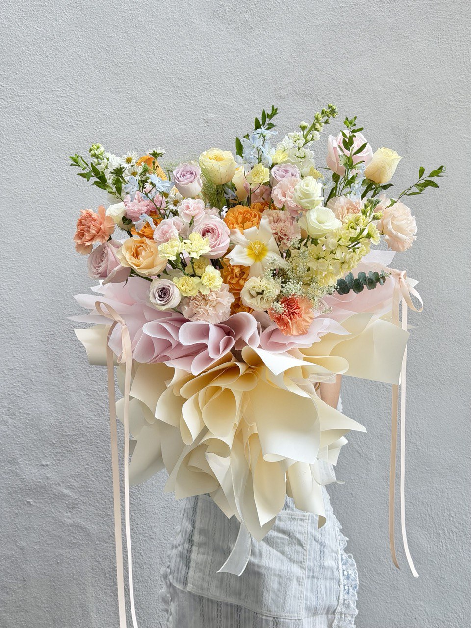 A girl holding a mixed colour roses with white tulip, pink rose, lilac rose, delphinium blue and fillers witha ballet wrapping at hug and heart florist.