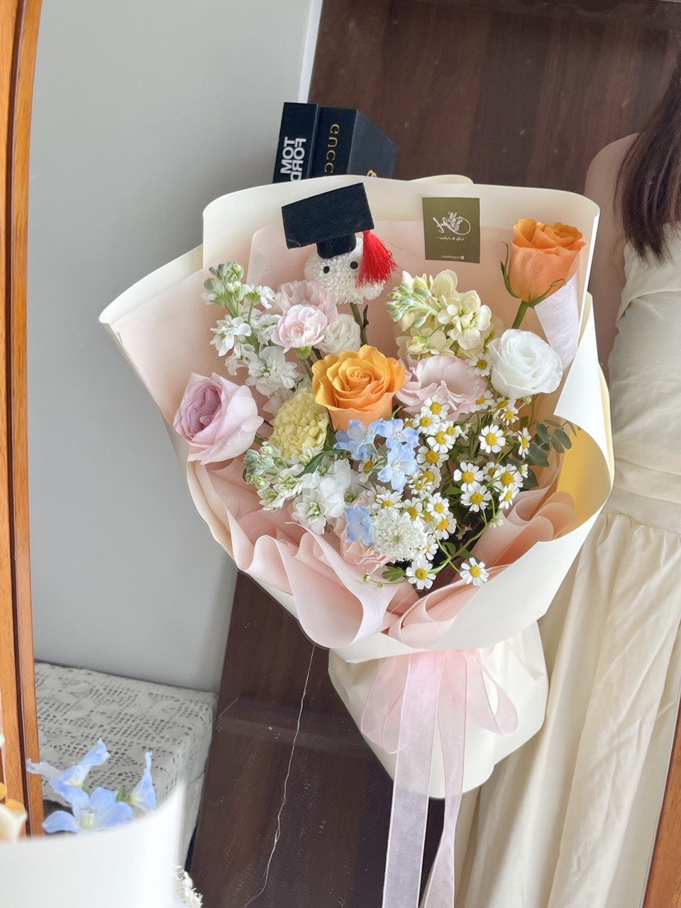 Bouquet of graduation flowers with a ping pong with graduation hat is held by a person infront of a mirror.