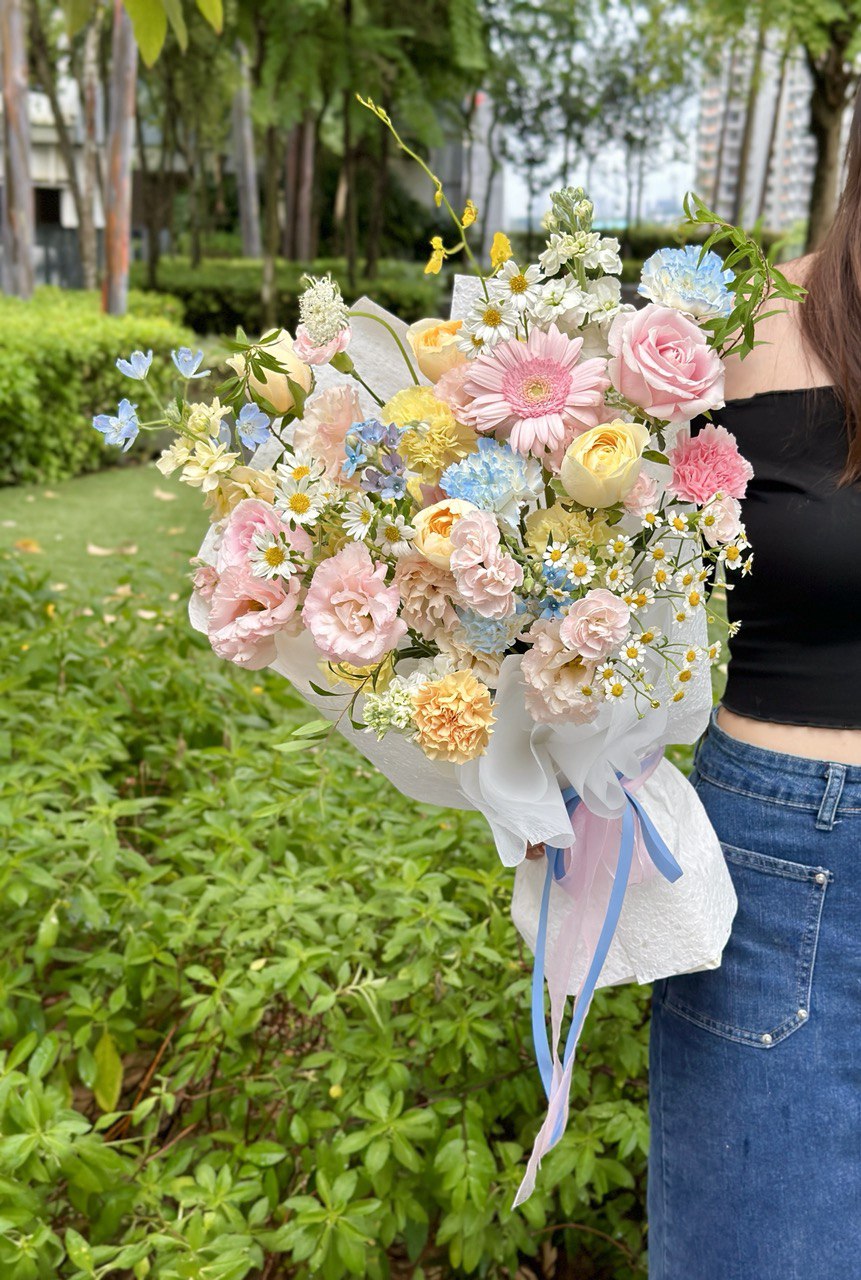 Person holding a large bouquet of flowers outdoors with greenery in the background.