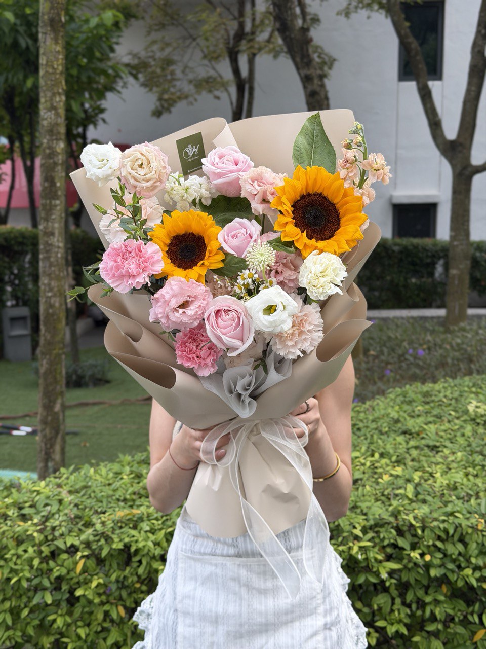 Person holding a bouquet of sunflower outdoors with greenery in the background at Sunway Geo.