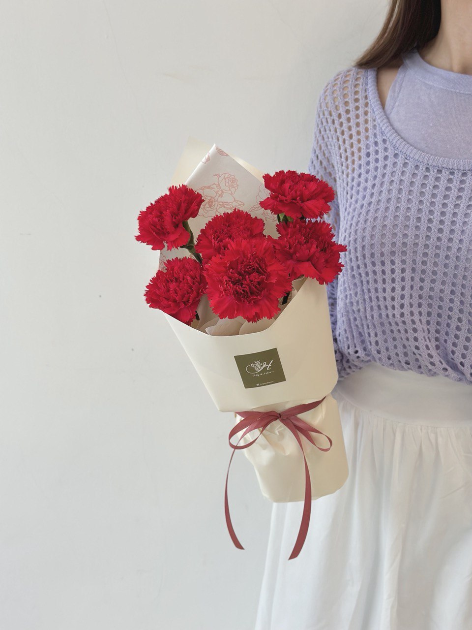 A girl is holding a red carnation bouquet for her mother during mother's day 2025