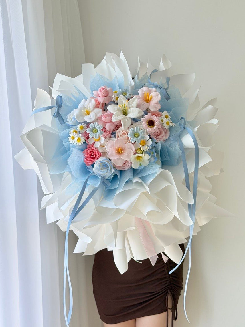 Elegant pastel soap flower bouquet with layered ballet wrap in blue and white, ideal for romantic or special occasions prepared by Hug and Heart Florist.