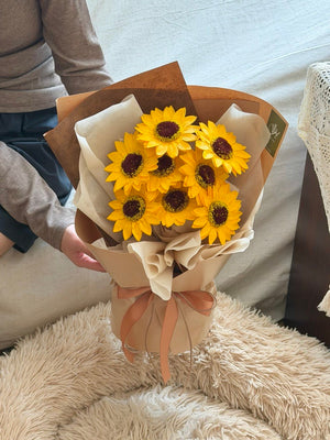 Bouquet of soap flwoer sunflowers wrapped in brown paper with a bow on a fluffy surface perfect for graduation flower.